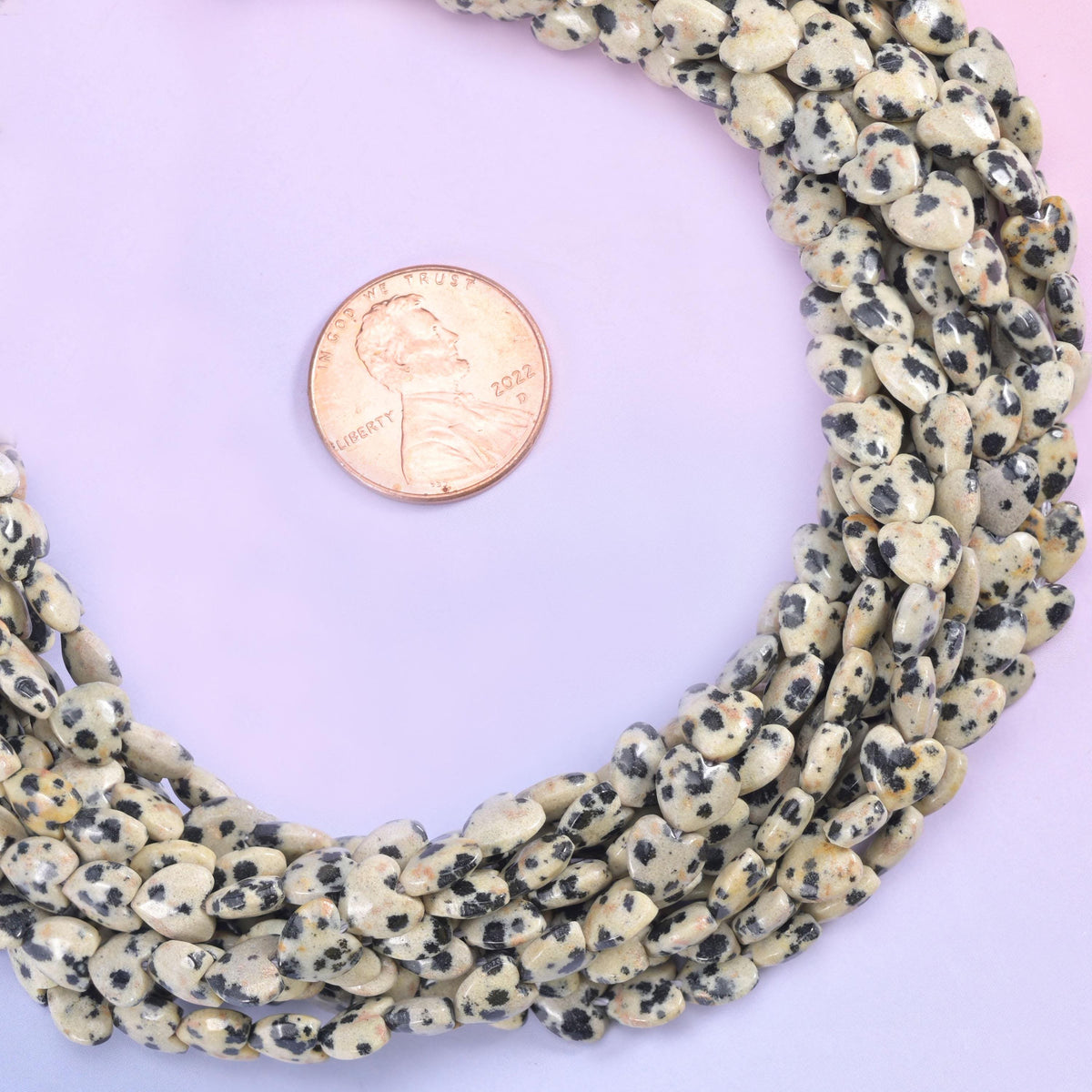 Dalmatian jasper heart beads coiled into a loop with a US penny alongside for size reference.