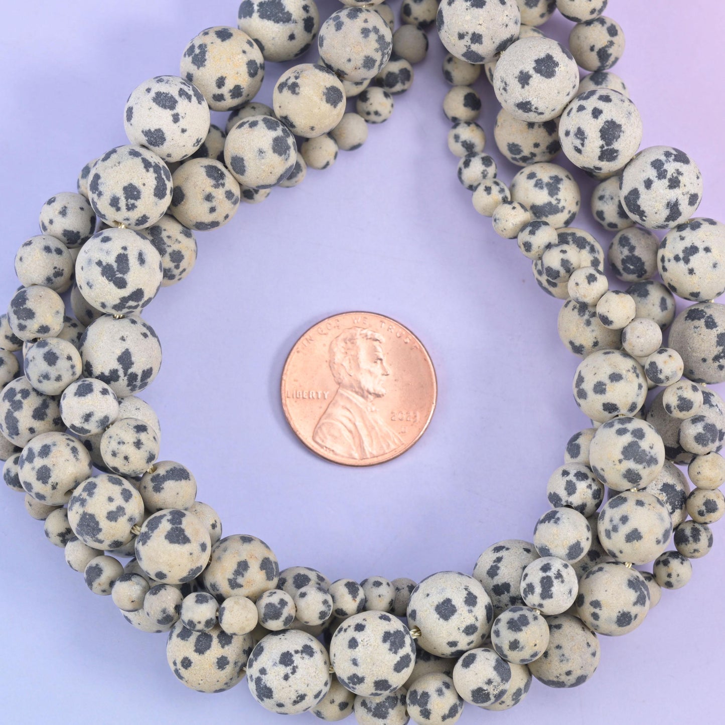 Dalmatian Jasper matte round bead strands coiled around a US penny for size reference