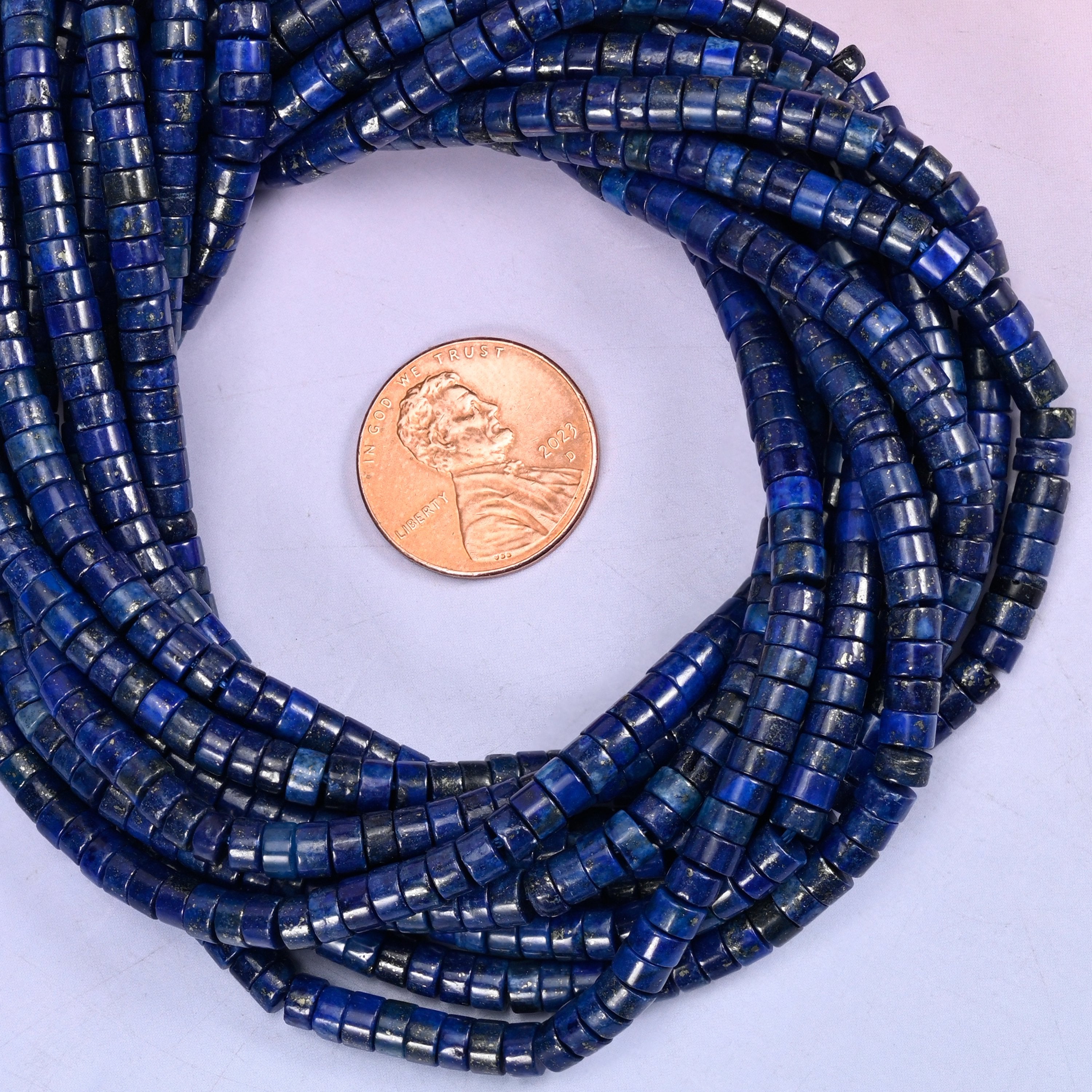 Dark Blue Lapis smooth heishi disc bead strands coiled around a US penny for size reference