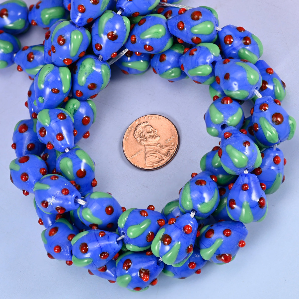 Dark Blue Red Dots Strawberry glass bead strands coiled around a US penny for size reference