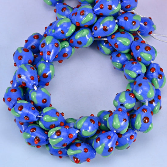 Dark Blue Red Dots Strawberry glass beads, close view of the coiled strands in deep blue with green leaves and raised red seed dots