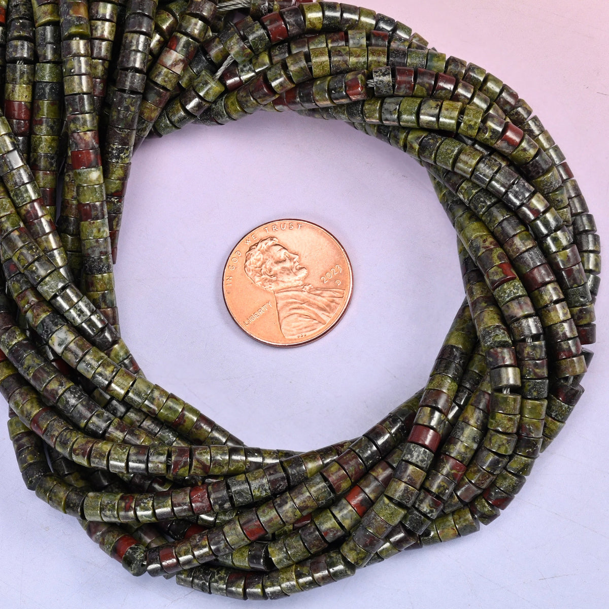 Dragon Blood Stone smooth heishi disc bead strands coiled around a US penny for size reference