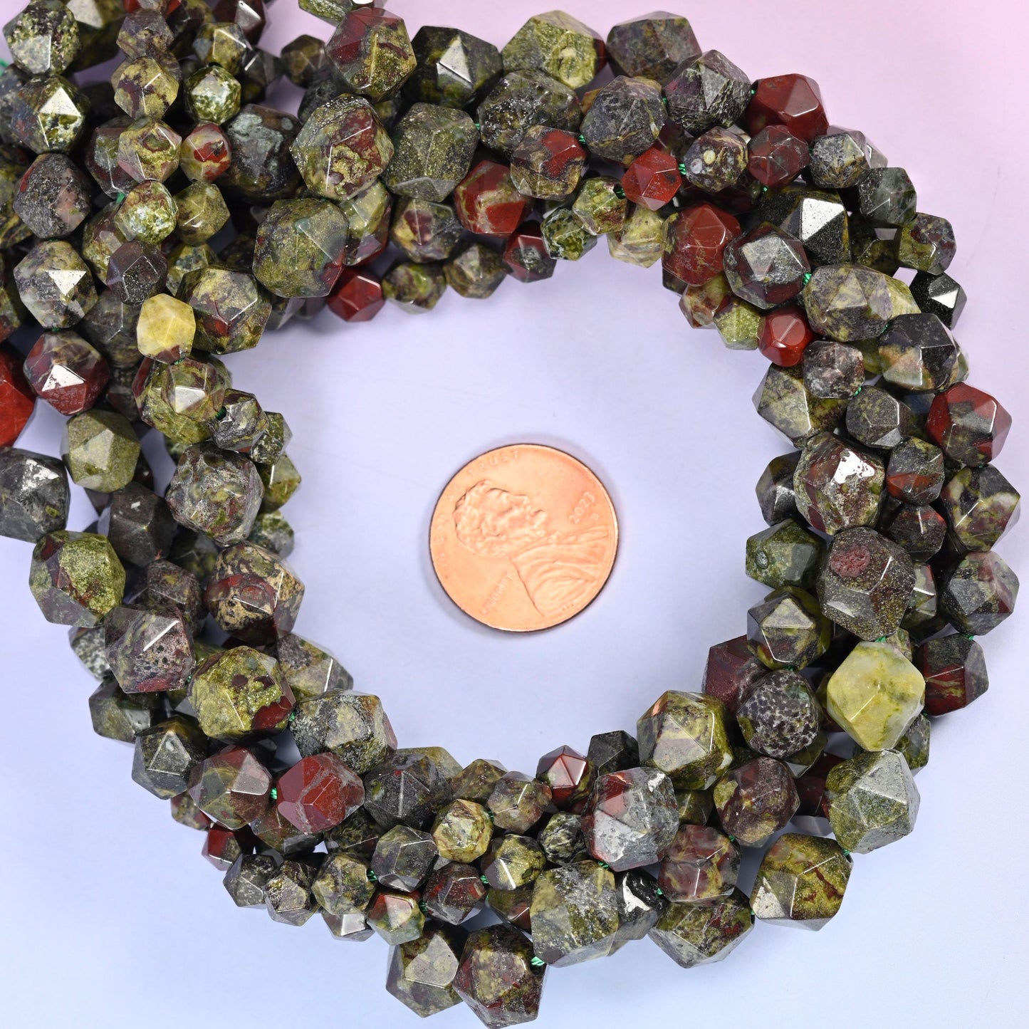 Dragon bloodstone faceted diamond star cut bead strands coiled around a US penny for size reference