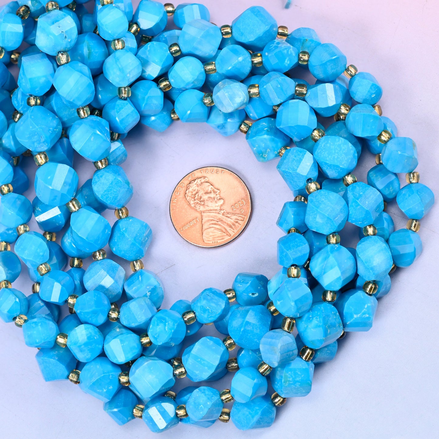 Dyed Blue Howlite faceted spiral twist bead strands coiled around a US penny for size reference