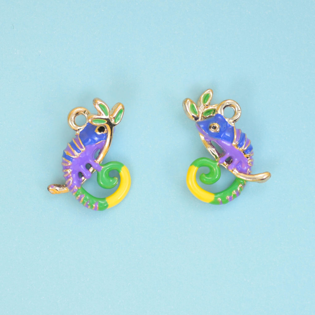 Two enamel chameleon charms side by side on a pale blue ground