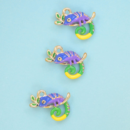 Three enamel chameleon charms with purple bodies and green and yellow curled tails on a pale blue ground