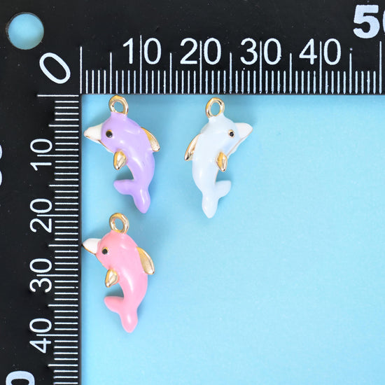 Lilac, white and pink enamel dolphin charms beside a millimetre ruler for scale