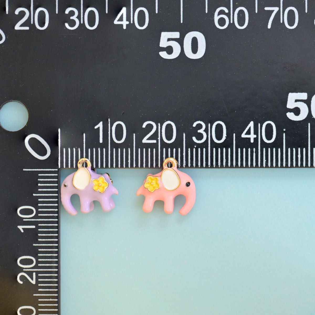 Lilac and pink enamel elephant charms beside a millimetre ruler for scale