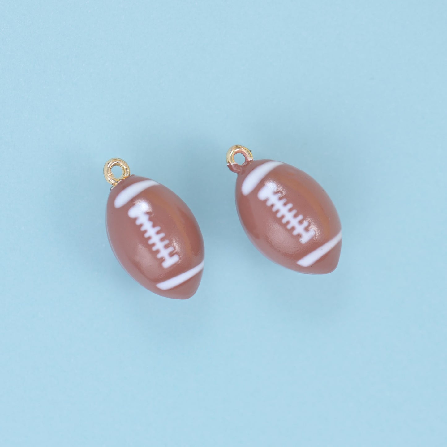 Two brown enamel football charms angled on a pale blue ground