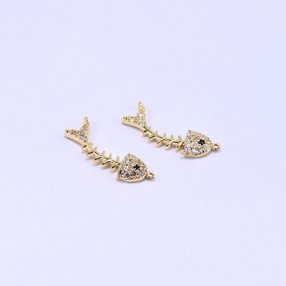 Three gold-plated fishbone zircon charms on a lilac background