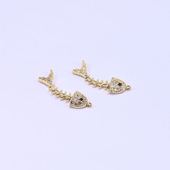 Three gold-plated fishbone zircon charms on a lilac background