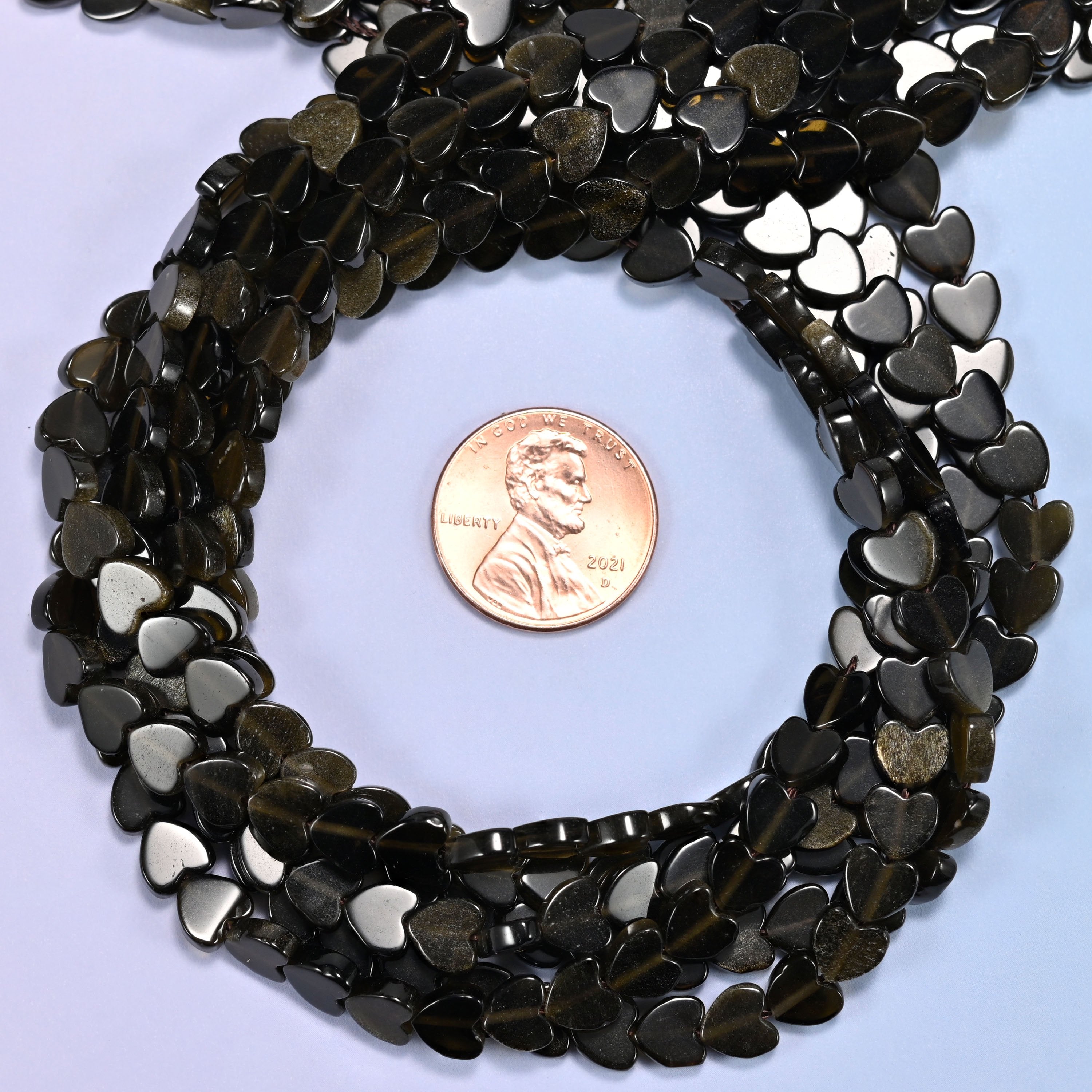 Gold Obsidian flat heart bead strands coiled around a US penny for size reference