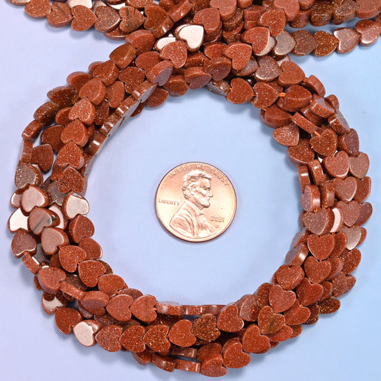 Gold Sandstone flat heart bead strands coiled around a US penny for size reference