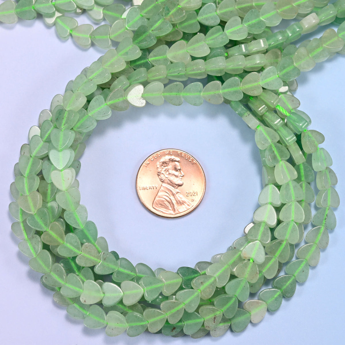 Green Aventurine flat heart bead strands coiled around a US penny for size reference