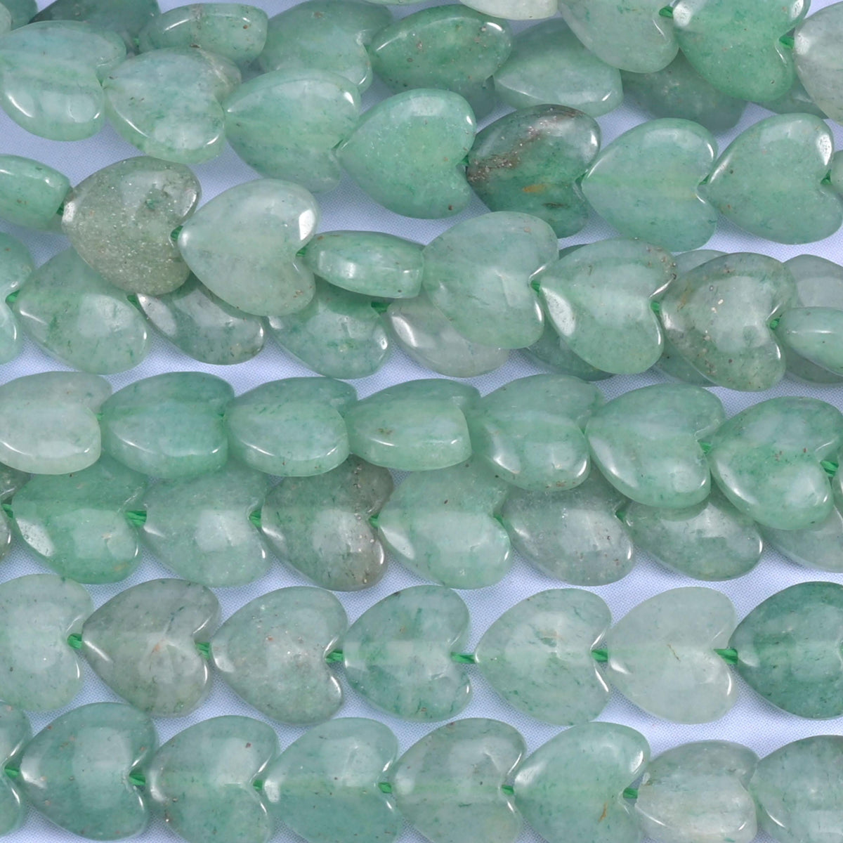 Green aventurine heart beads, close view of several strands showing the puffed heart shape.