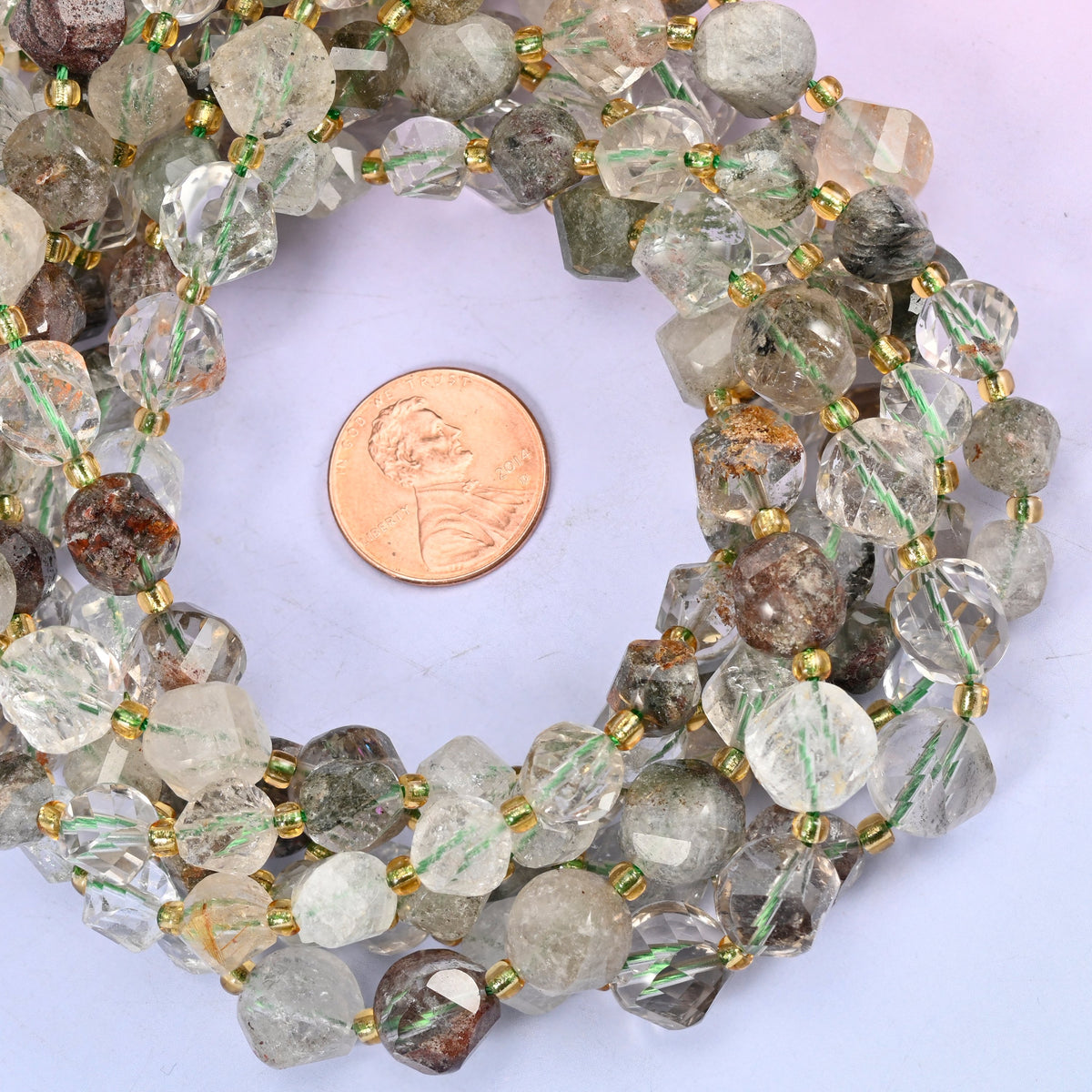 Green Phantom Quartz faceted spiral twist bead strands coiled around a US penny for size reference