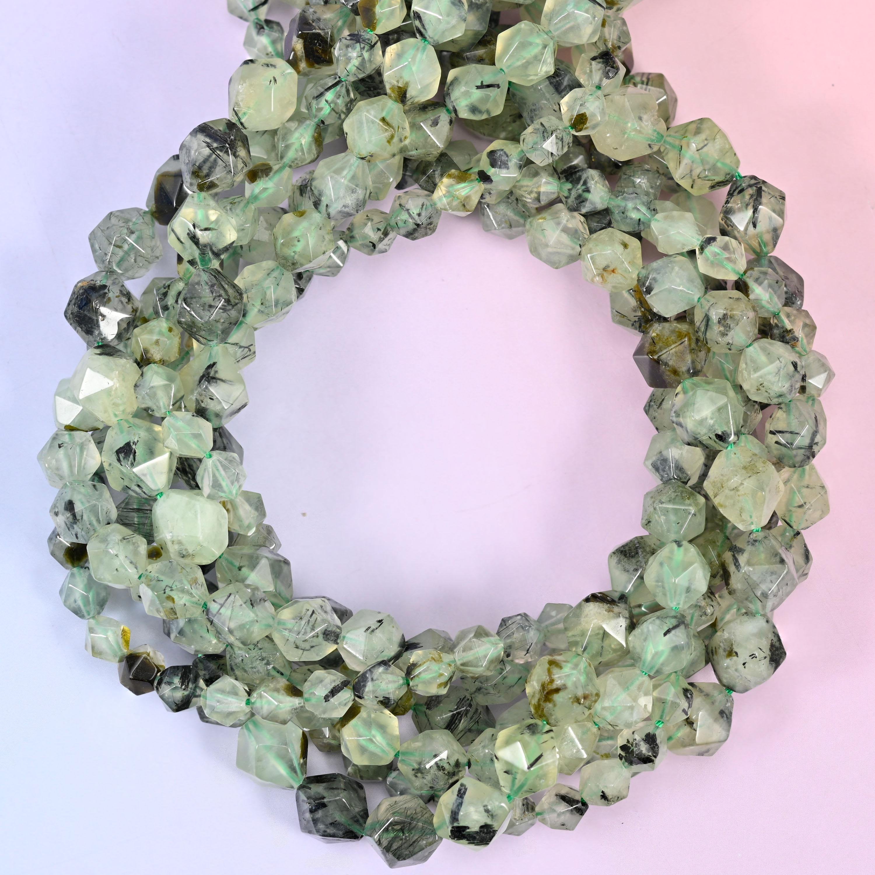 Green prehnite faceted diamond star cut beads, strands coiled into a ring showing the pale green stone and its dark speckling