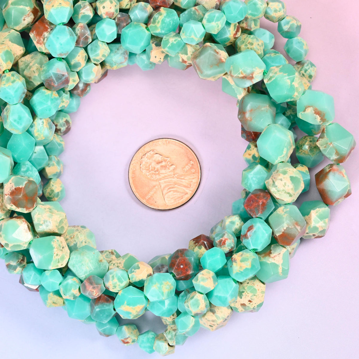 Green Shoushan stone faceted diamond star cut bead strands coiled around a US penny for size reference