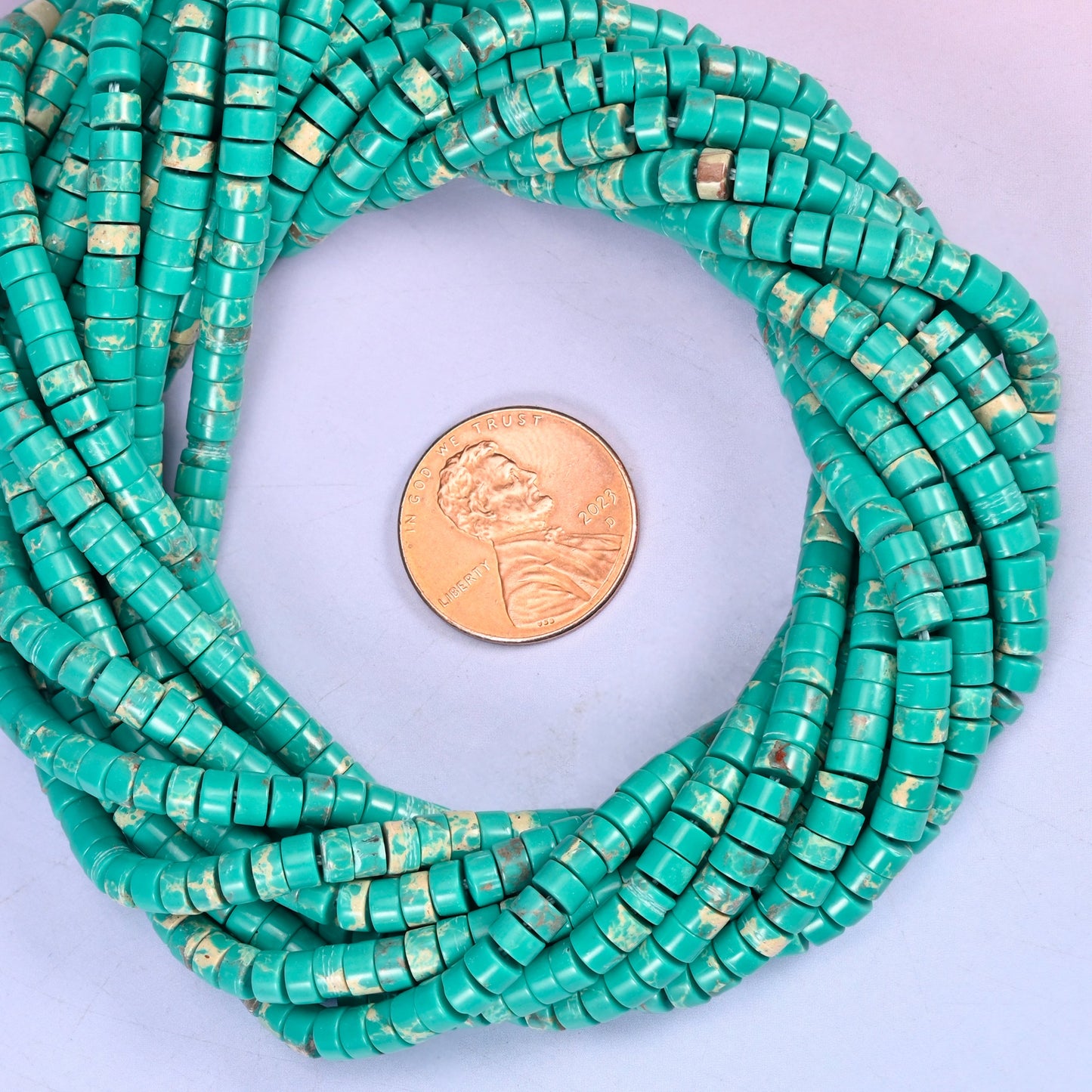 Green Shoushan Stone smooth heishi disc bead strands coiled around a US penny for size reference