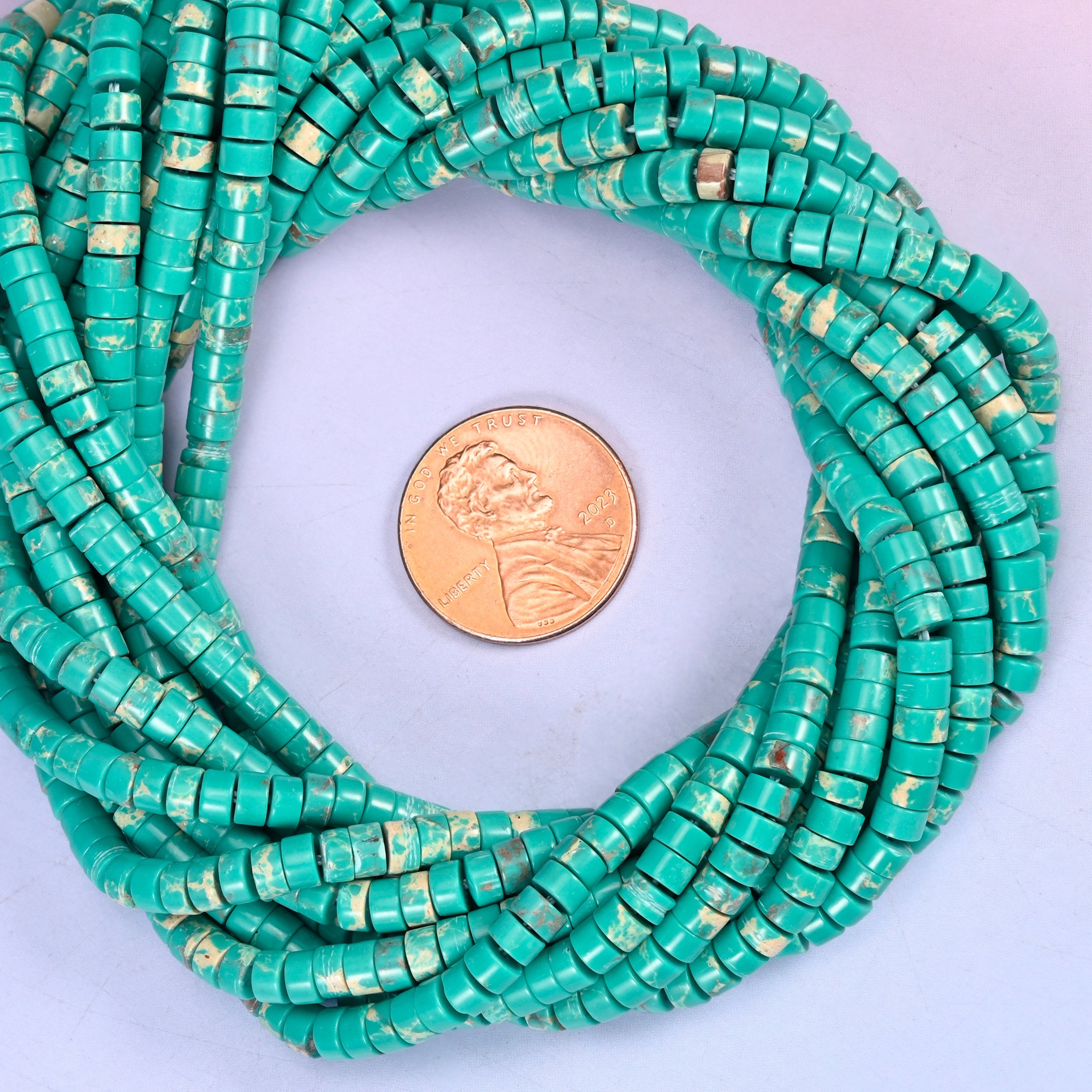 Green Shoushan Stone smooth heishi disc bead strands coiled around a US penny for size reference
