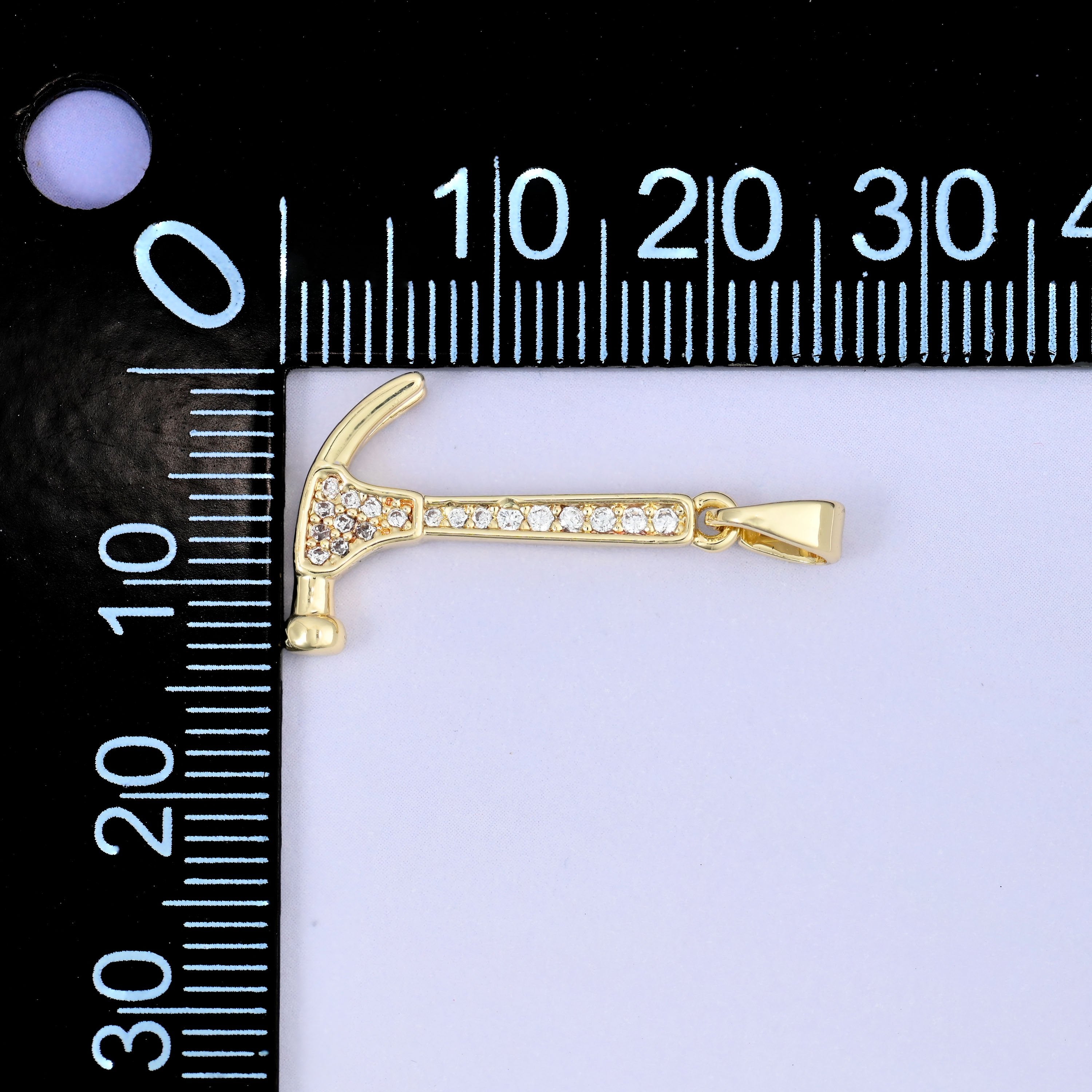 A hammer zircon charm shown lying sideways beside a millimetre ruler for scale