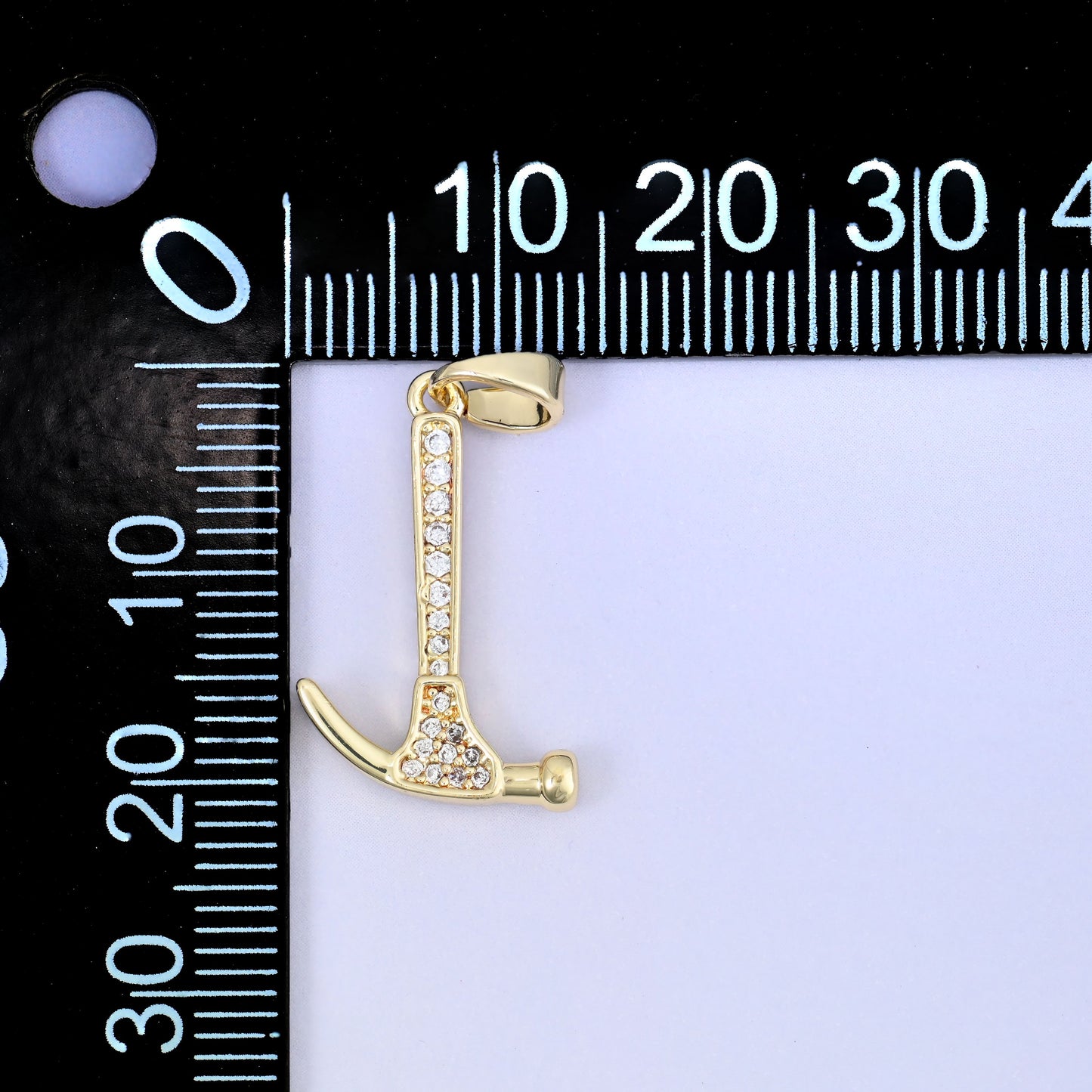 A hammer zircon charm shown upright beside a millimetre ruler for scale