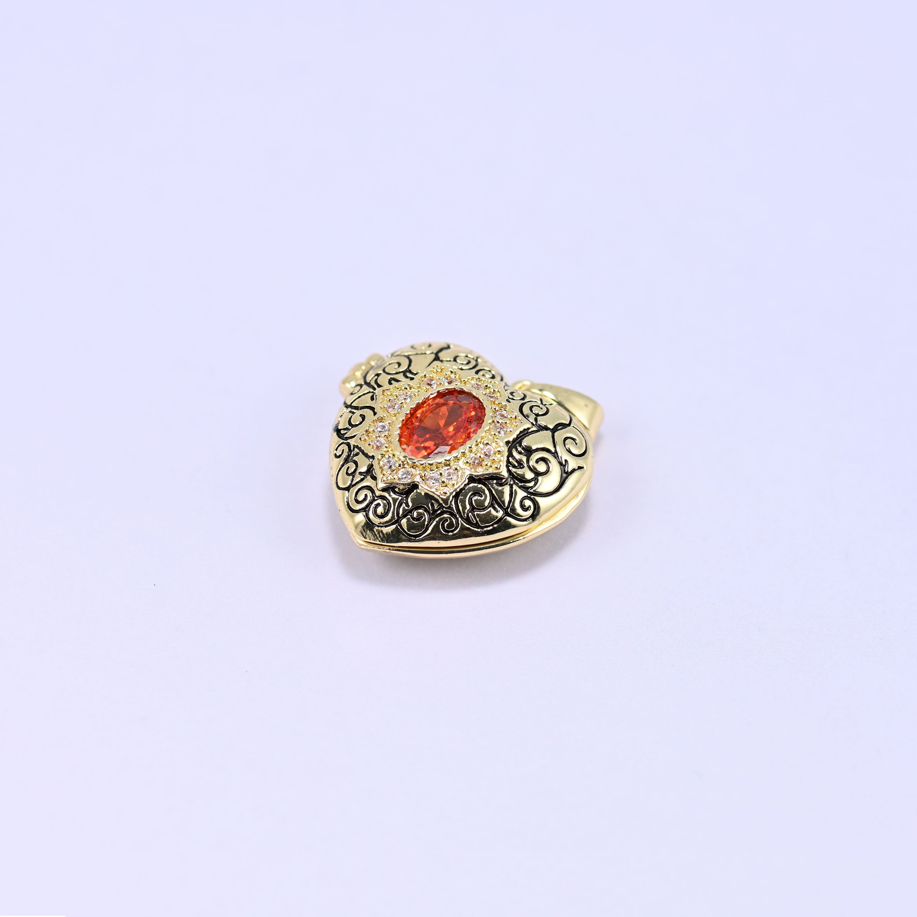 A heart locket charm with a filigree front and an orange oval stone, shown alone on a lilac background