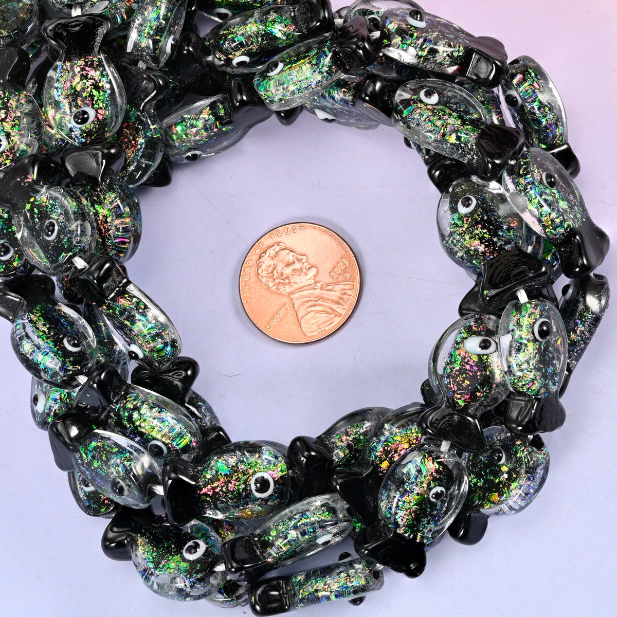 Iridescent Black Green Fish glass bead strands coiled around a US penny for size reference