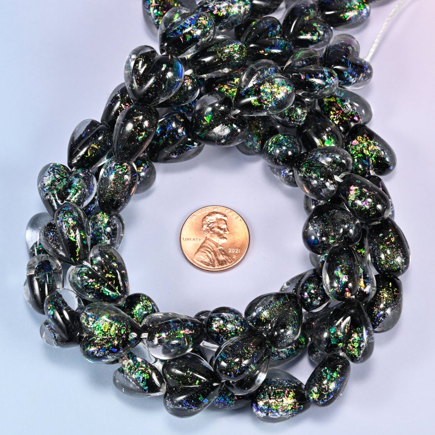 Iridescent Black Green Heart glass bead strands coiled around a US penny for size reference