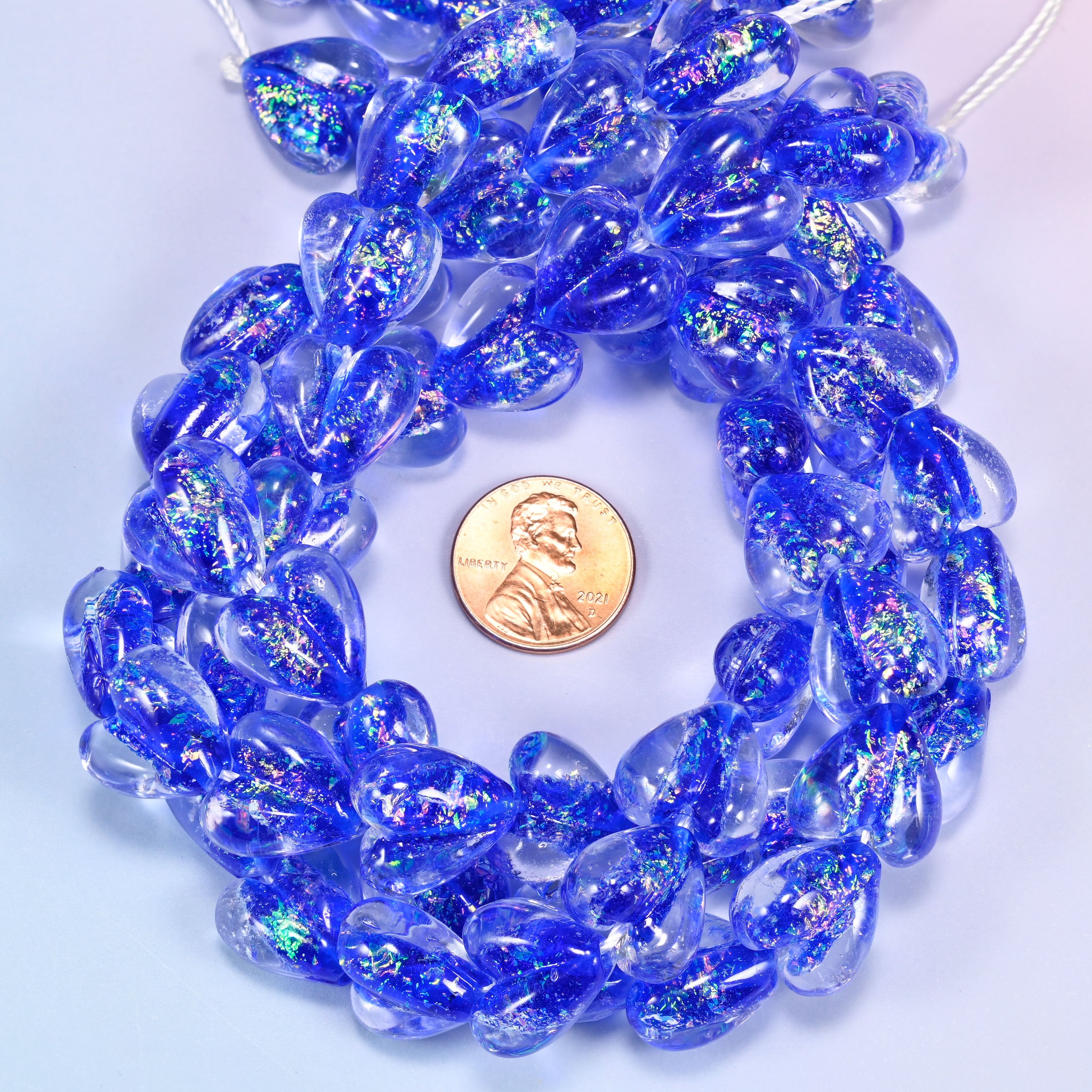 Iridescent dark blue heart glass bead strands coiled around a US penny for size reference