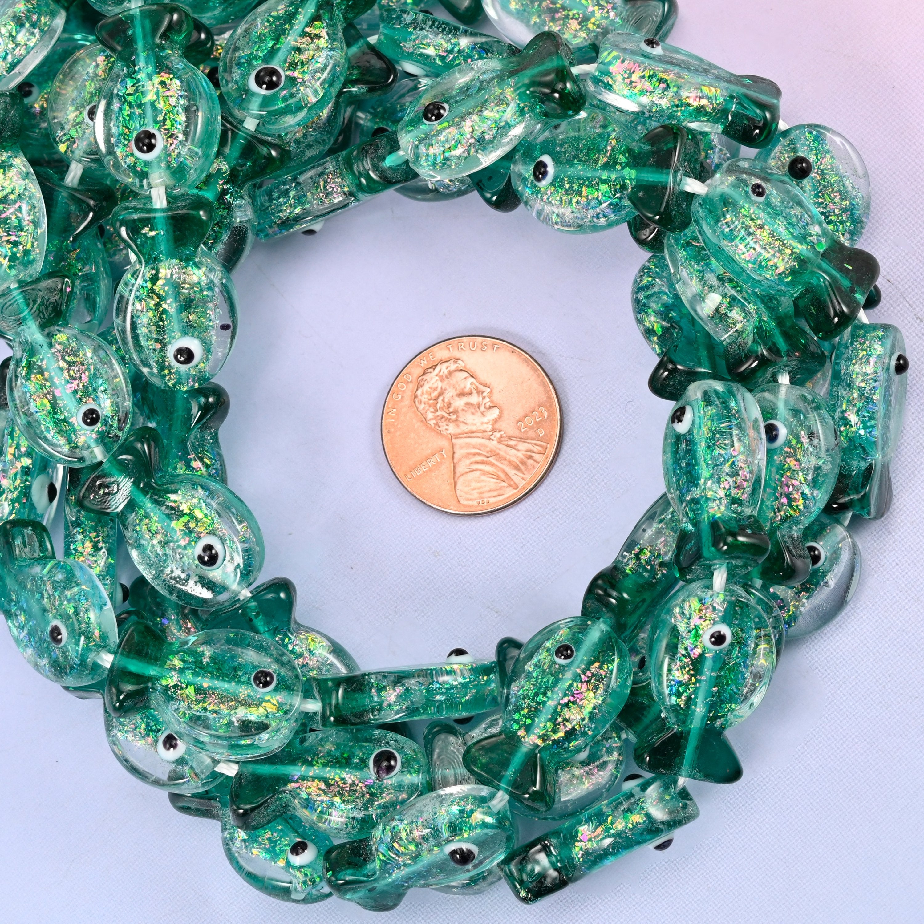 Iridescent Green Fish glass bead strands coiled around a US penny for size reference