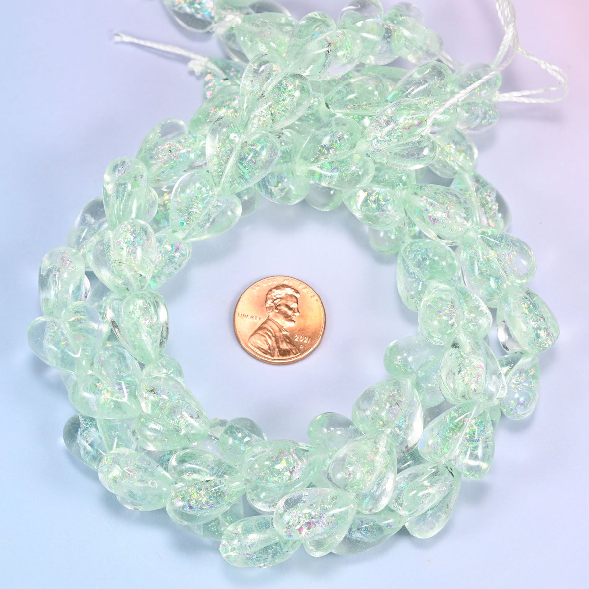 Iridescent Light Green Heart glass bead strands coiled around a US penny for size reference
