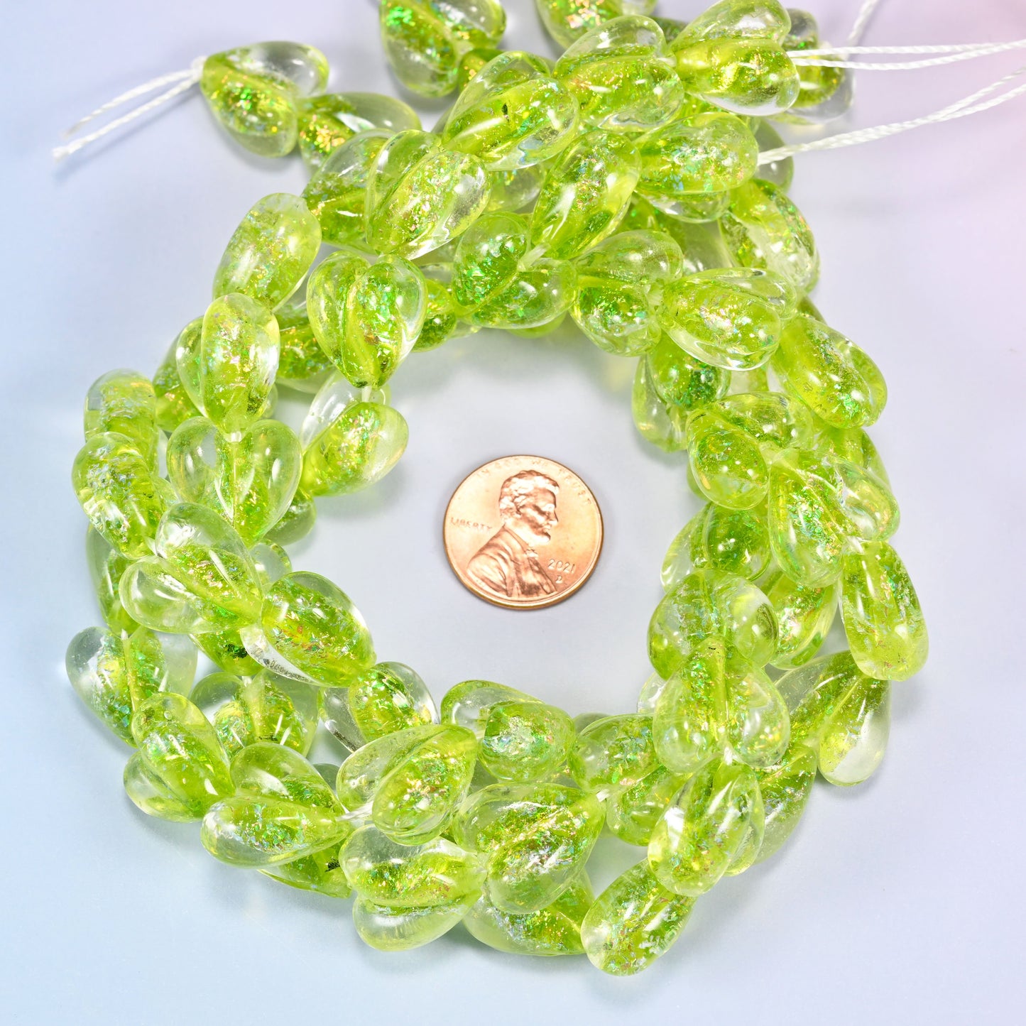 Iridescent Lime Green Heart glass bead strands coiled around a US penny for size reference