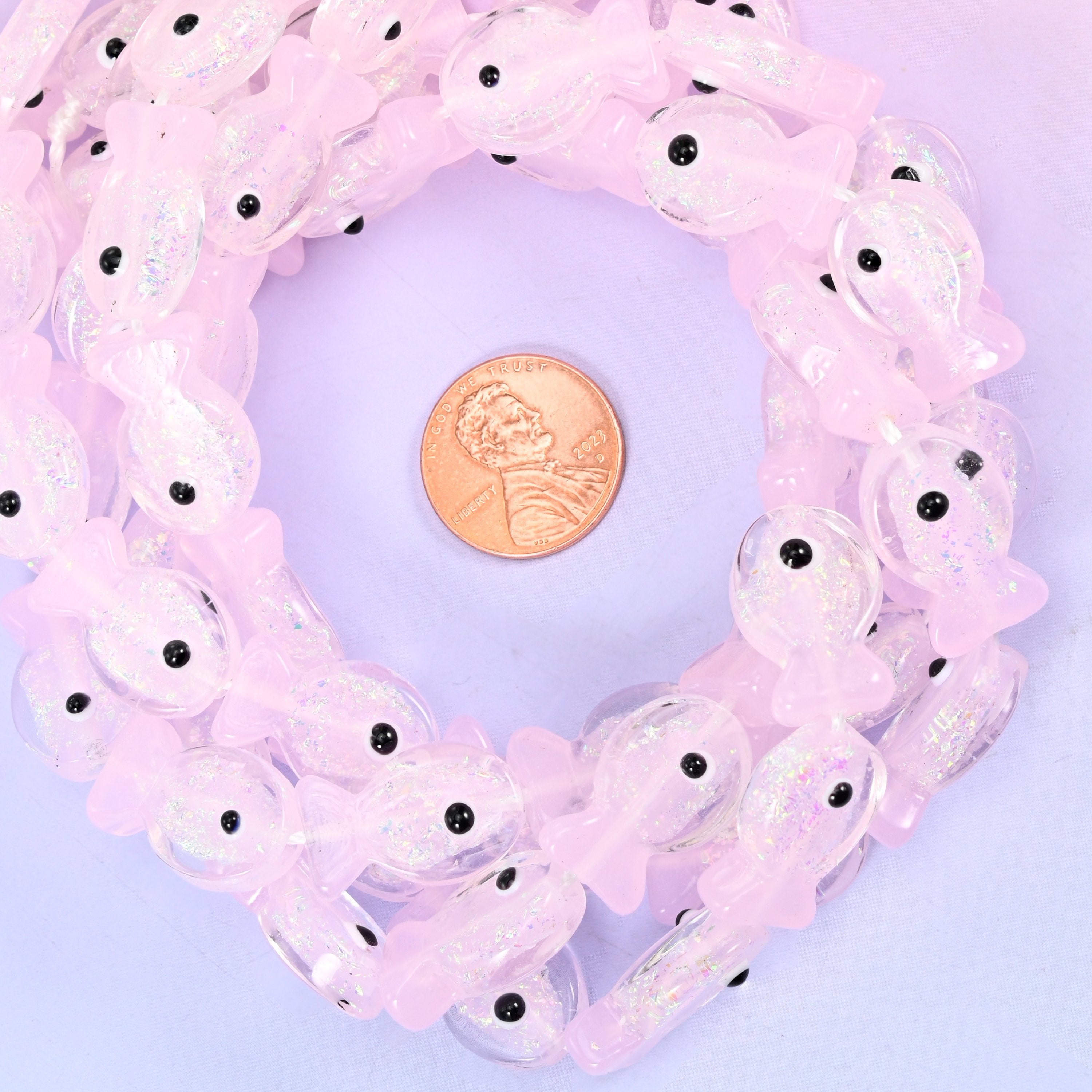 Iridescent Pink Fish glass bead strands coiled around a US penny for size reference