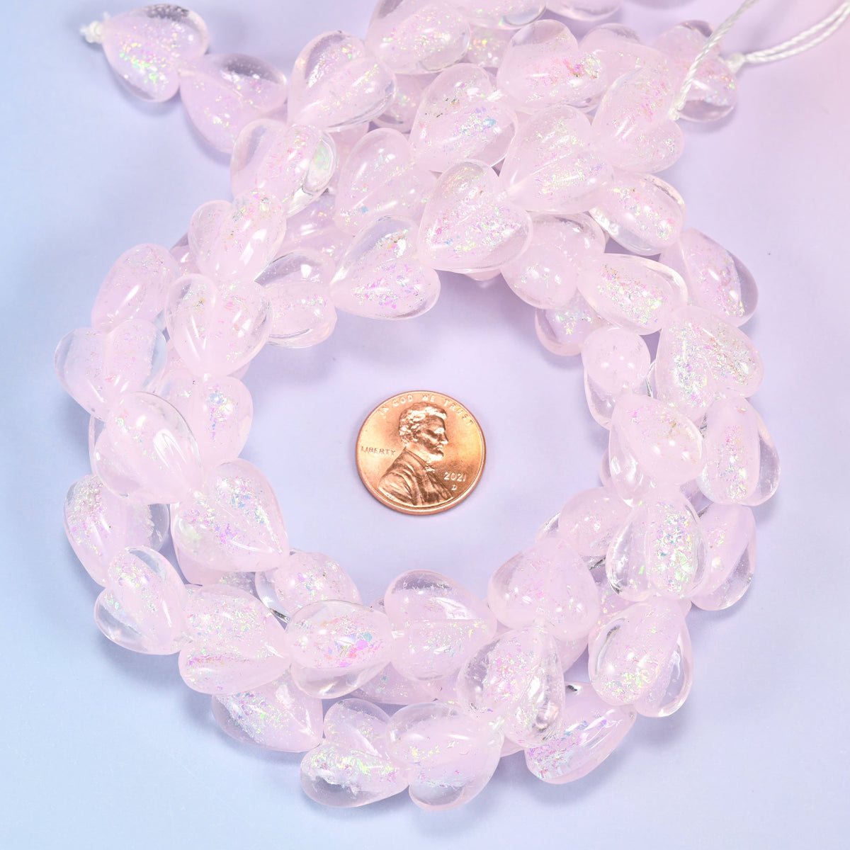 Iridescent pink heart glass bead strands coiled around a US penny for size reference