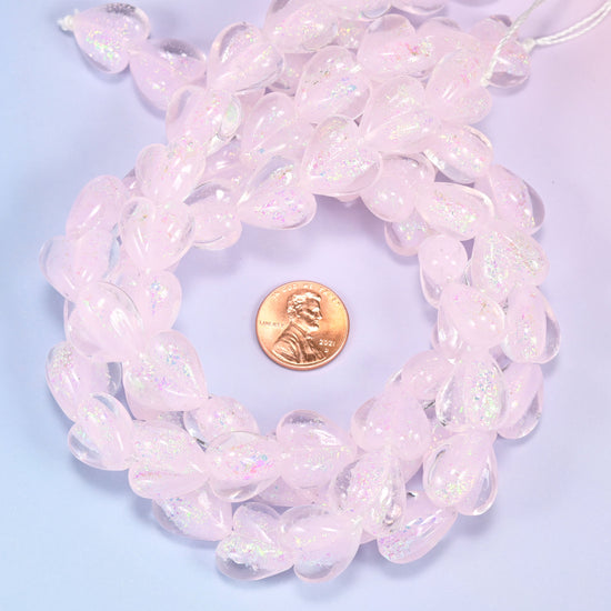 Iridescent pink heart glass bead strands coiled around a US penny for size reference
