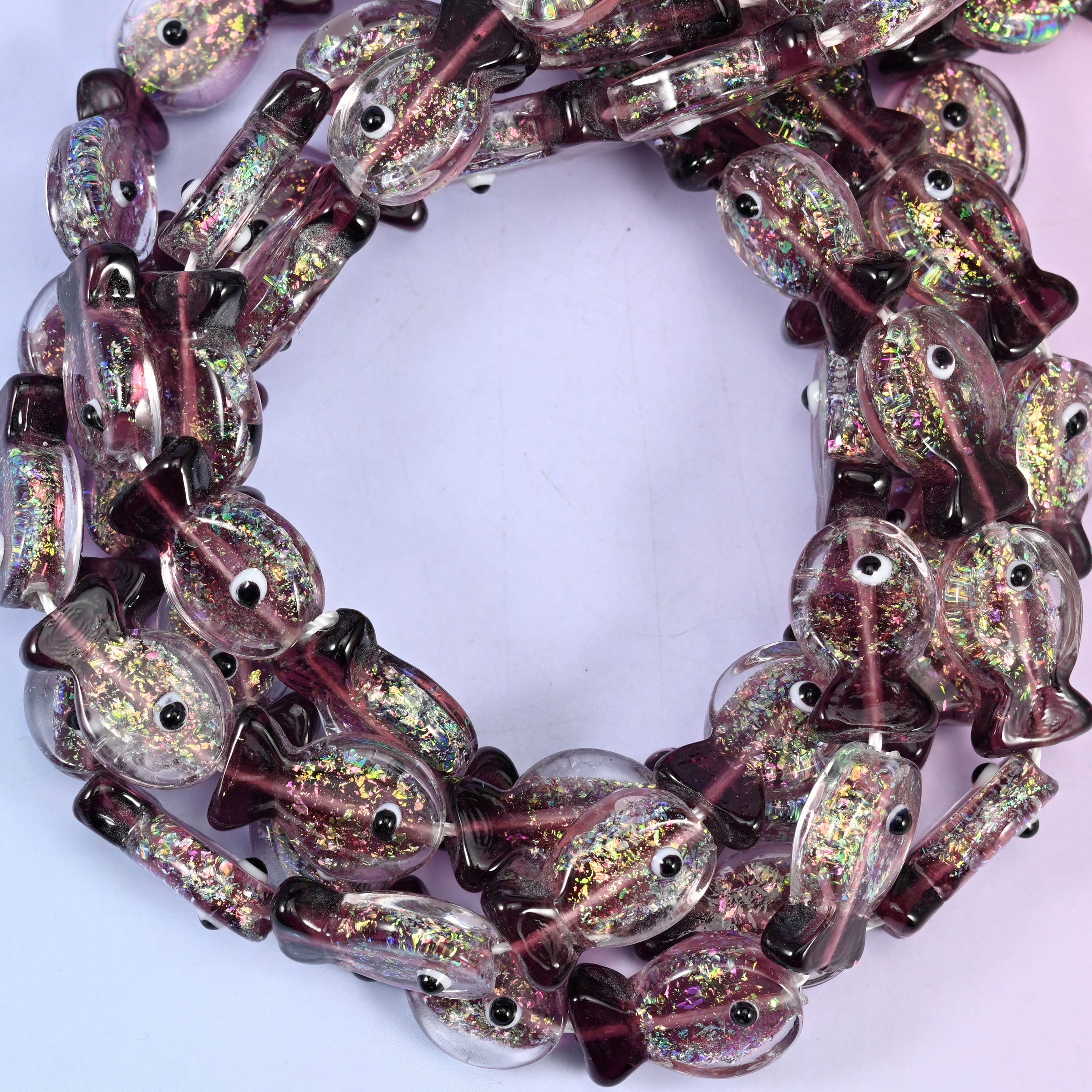 Iridescent Purple Fish glass beads, close view of the coiled strands in clear glass with purple fins and gold glitter inclusions