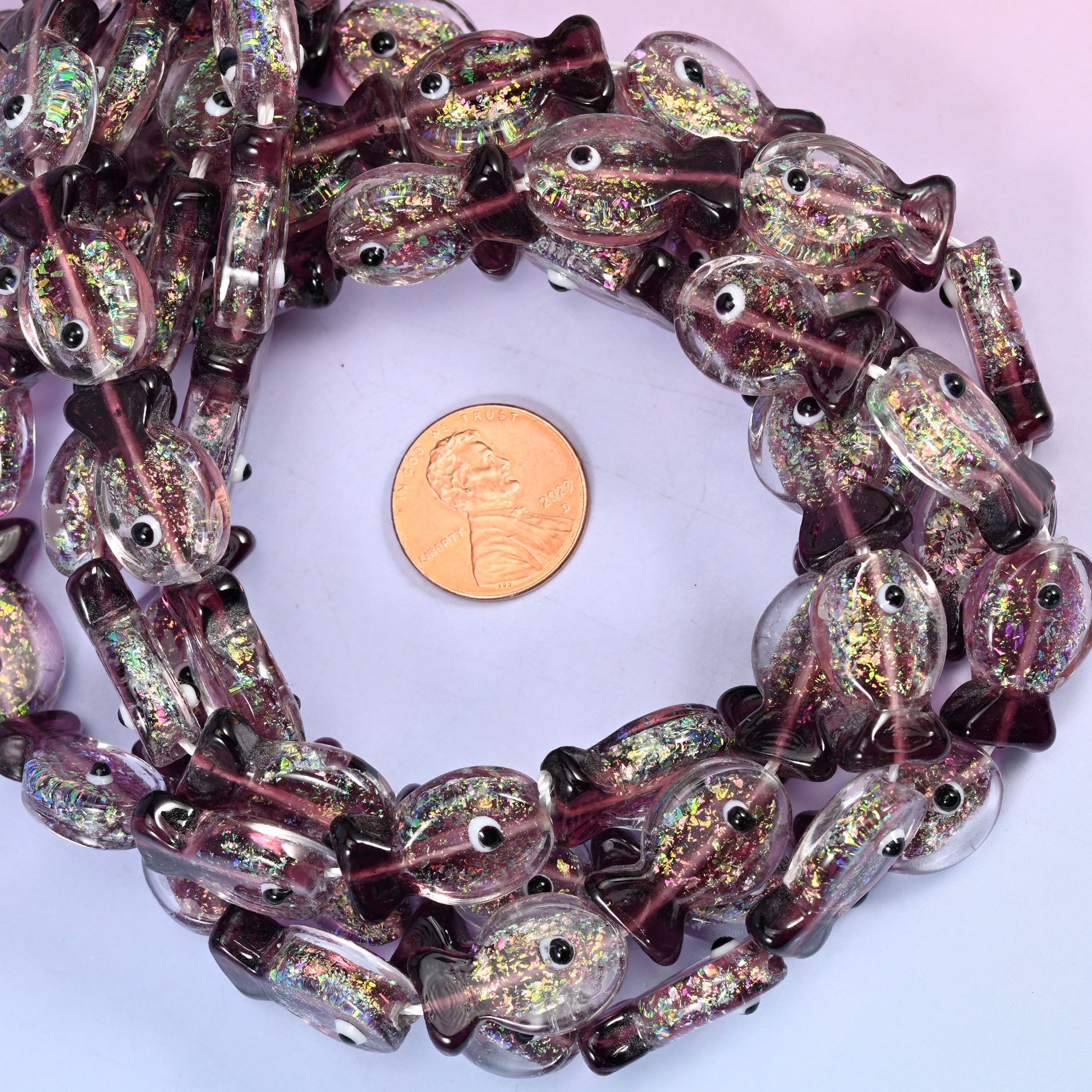 Iridescent Purple Fish glass bead strands coiled around a US penny for size reference