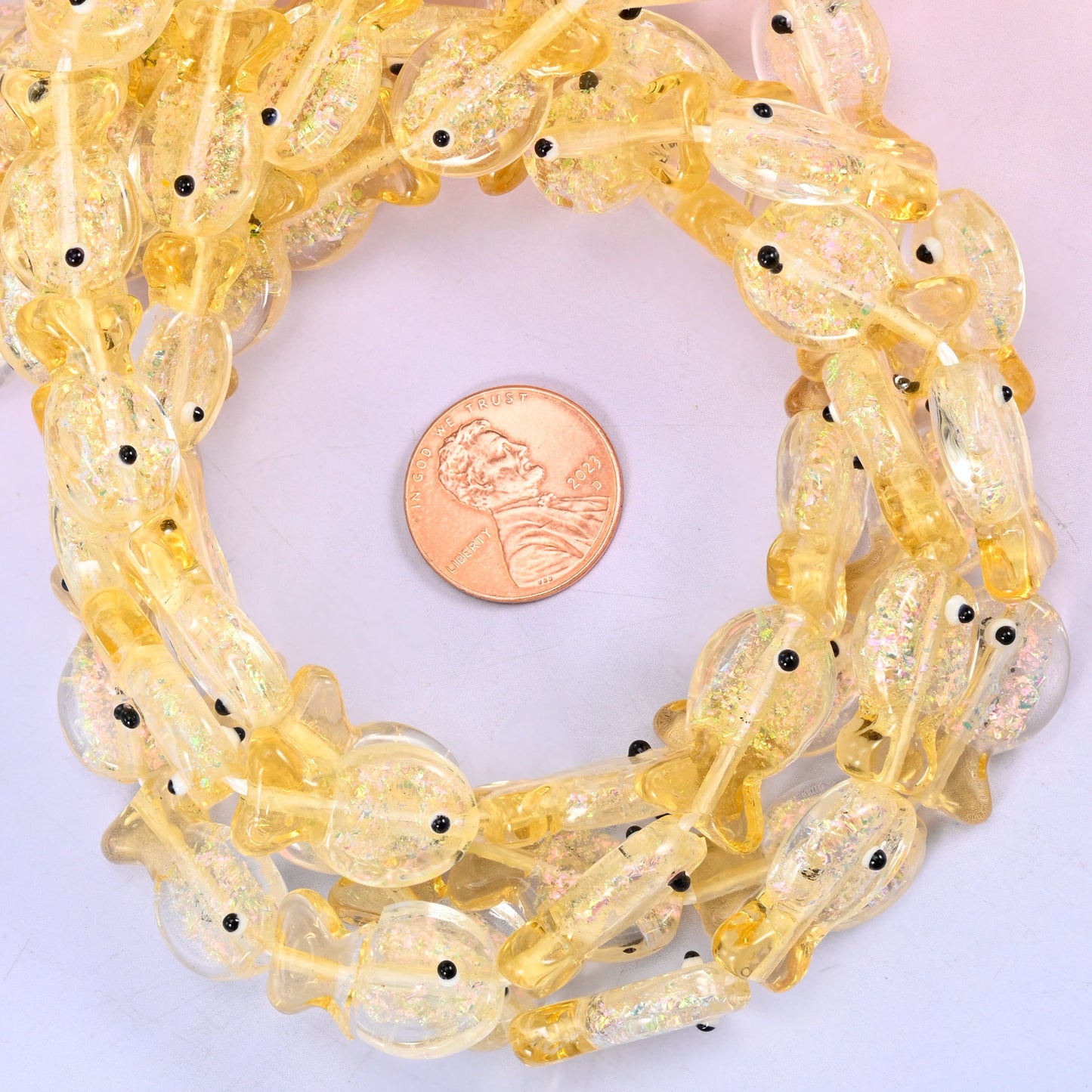 Iridescent Yellow Fish glass bead strands coiled around a US penny for size reference