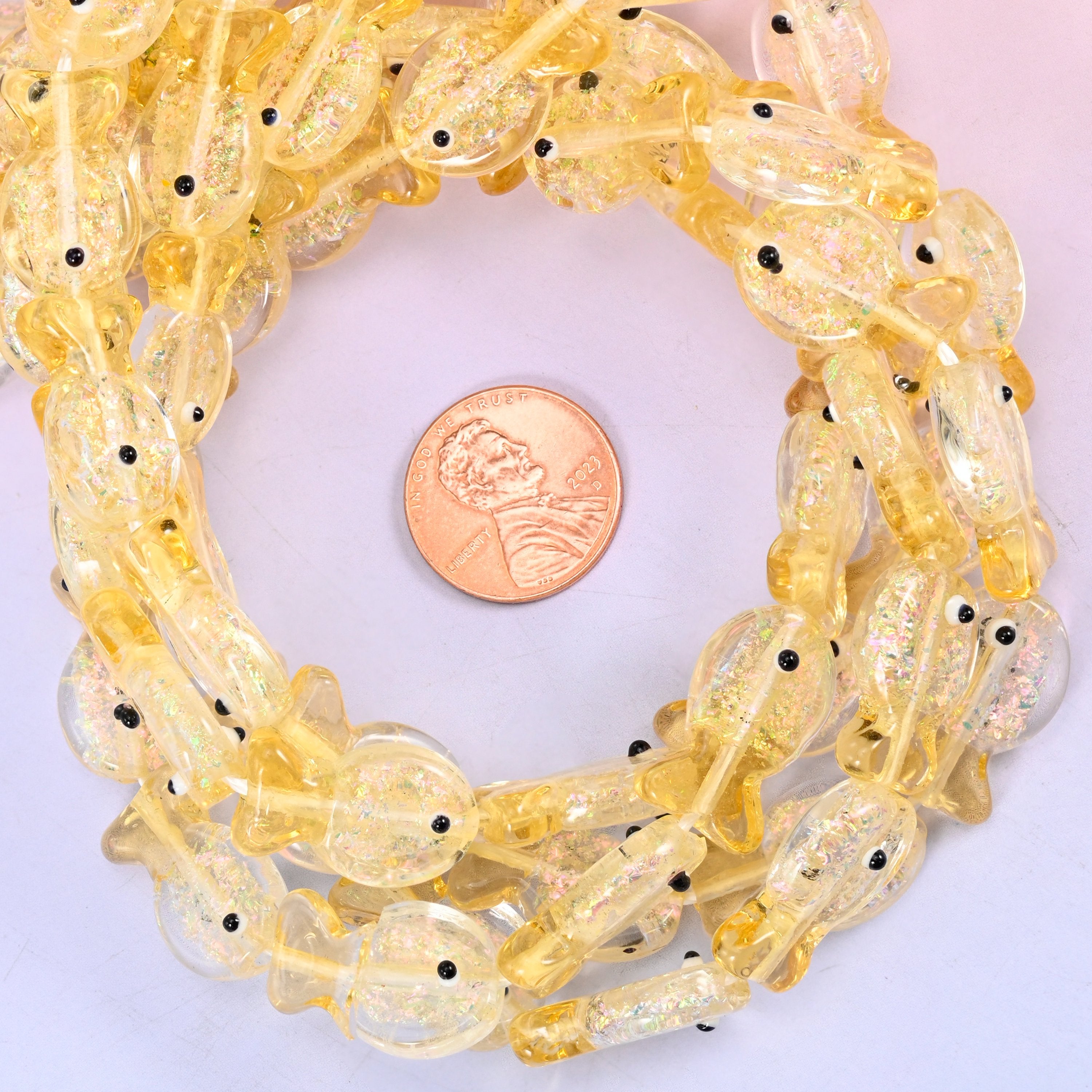 Iridescent Yellow Fish glass bead strands coiled around a US penny for size reference