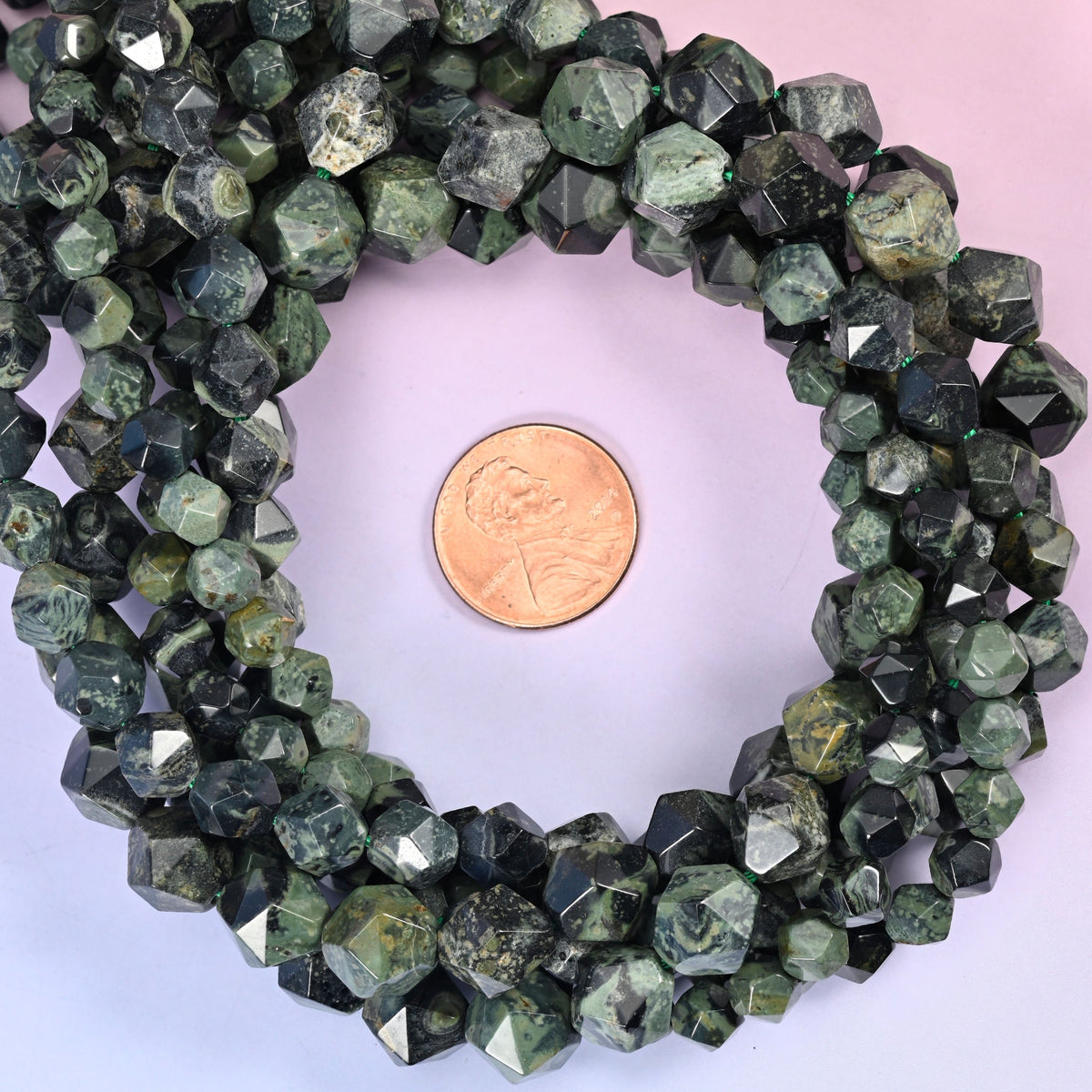 Kambaba jasper diamond star cut beads coiled around a US penny for size reference.