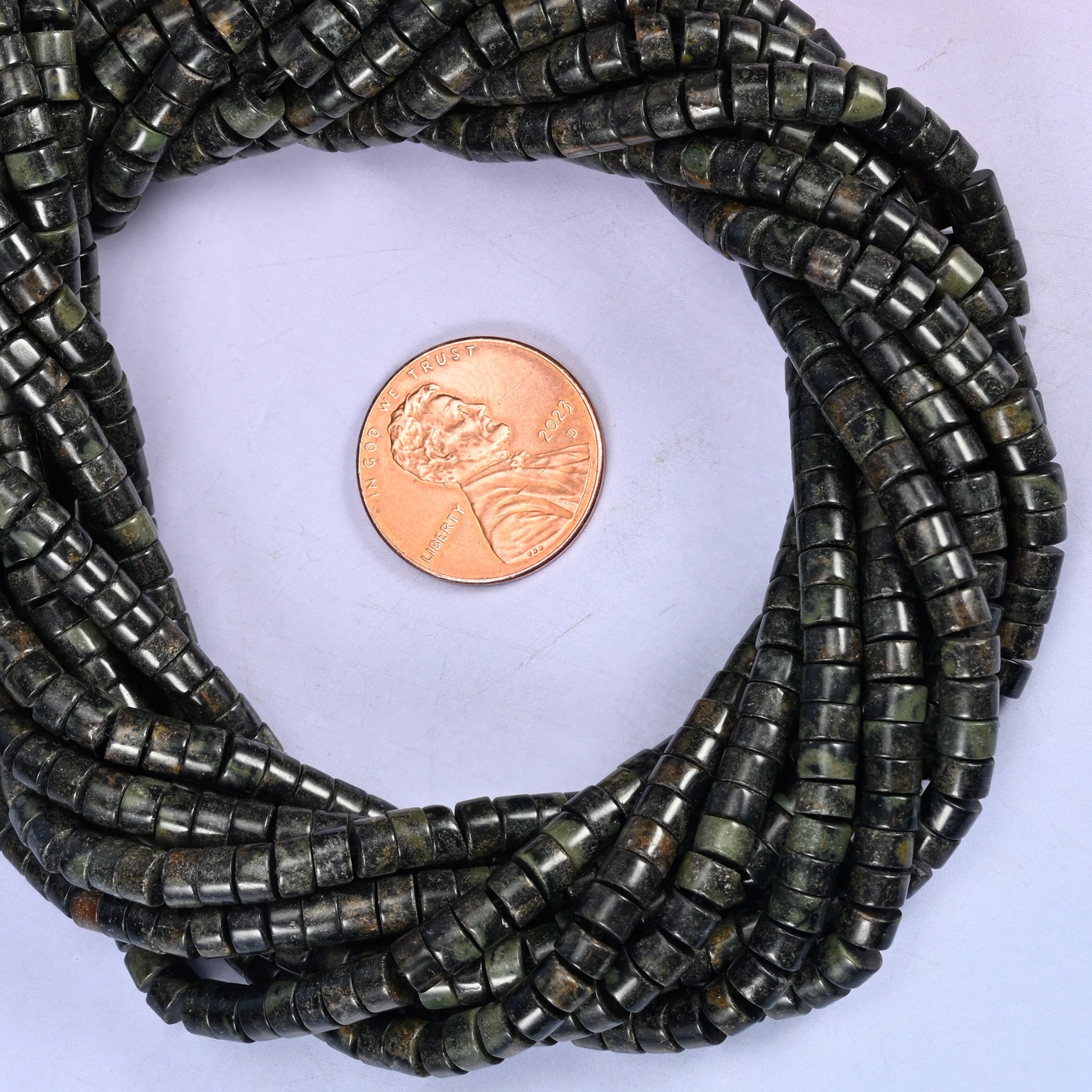 Kambaba Jasper smooth heishi disc bead strands coiled around a US penny for size reference