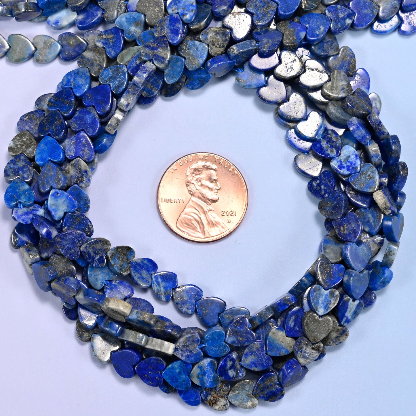 Lapis Lazuli flat heart bead strands coiled around a US penny for size reference