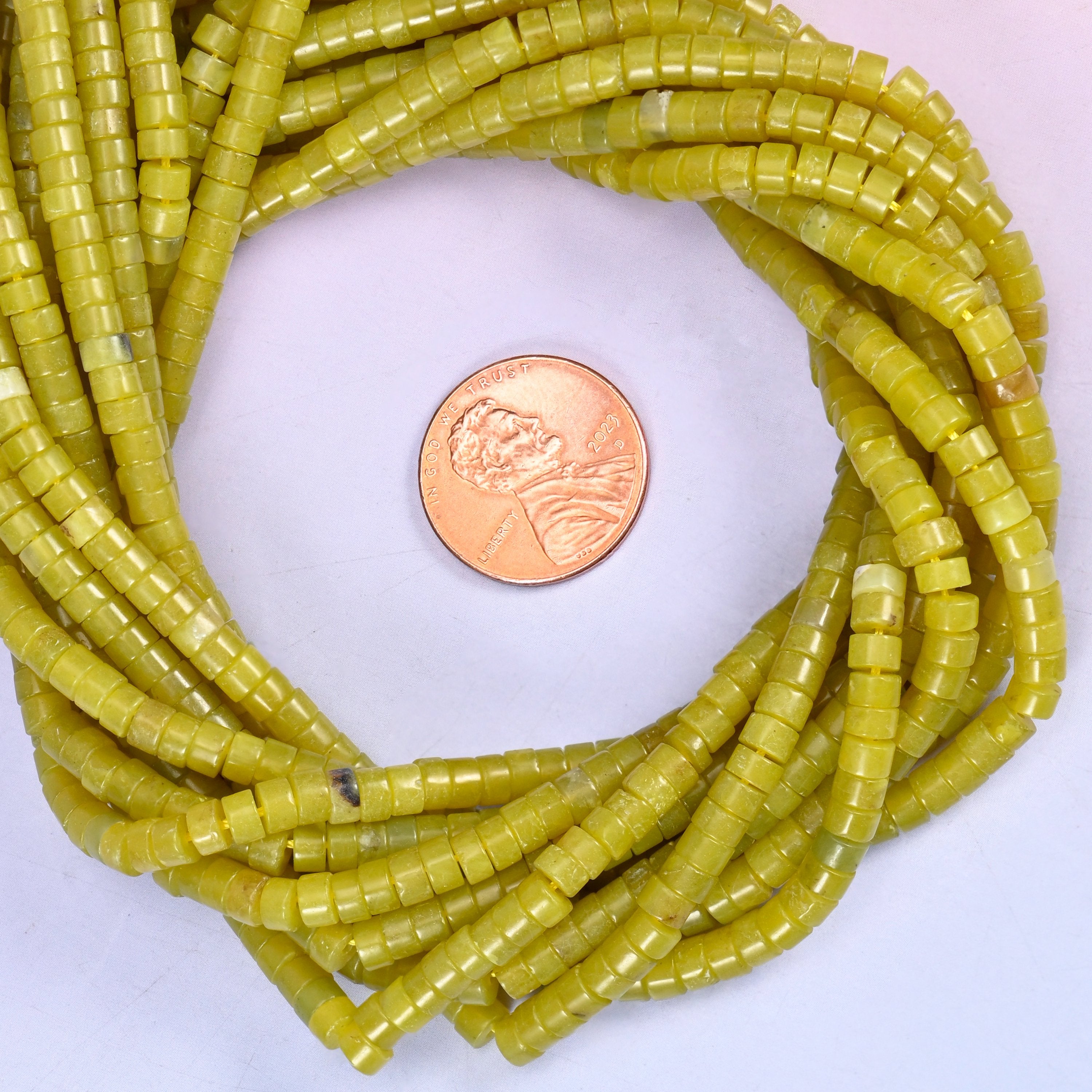 Lemon Jade smooth heishi disc bead strands coiled around a US penny for size reference