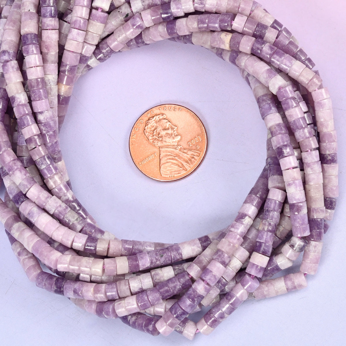 Lepidolite smooth heishi disc bead strands coiled around a US penny for size reference