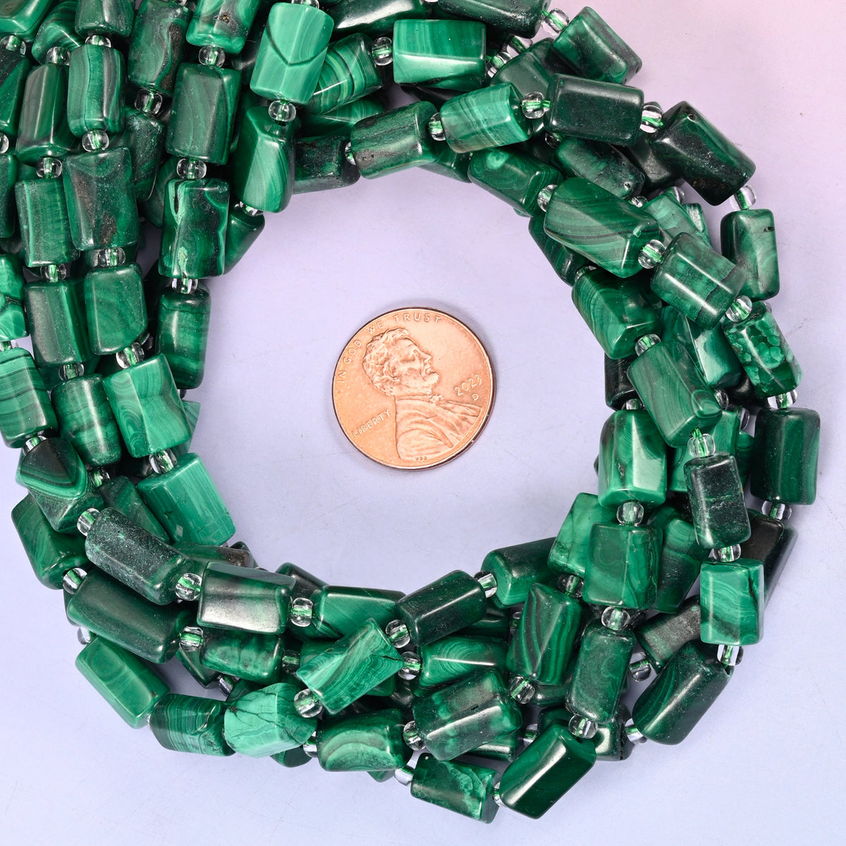 Malachite faceted tube bead strands coiled around a US penny for size reference