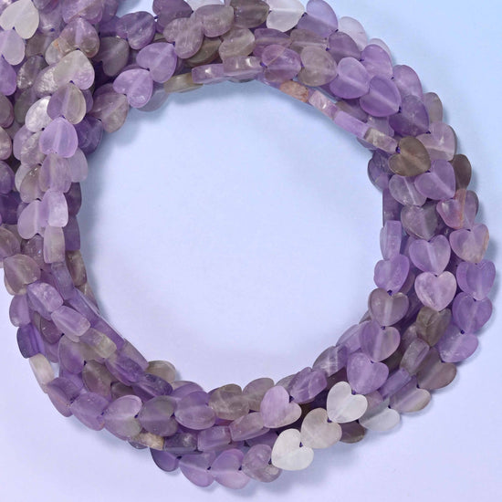 Amethyst flat heart-shaped beads draped diagonally across a fabric-covered cushion, 6mm matte beads, 15 inch strand