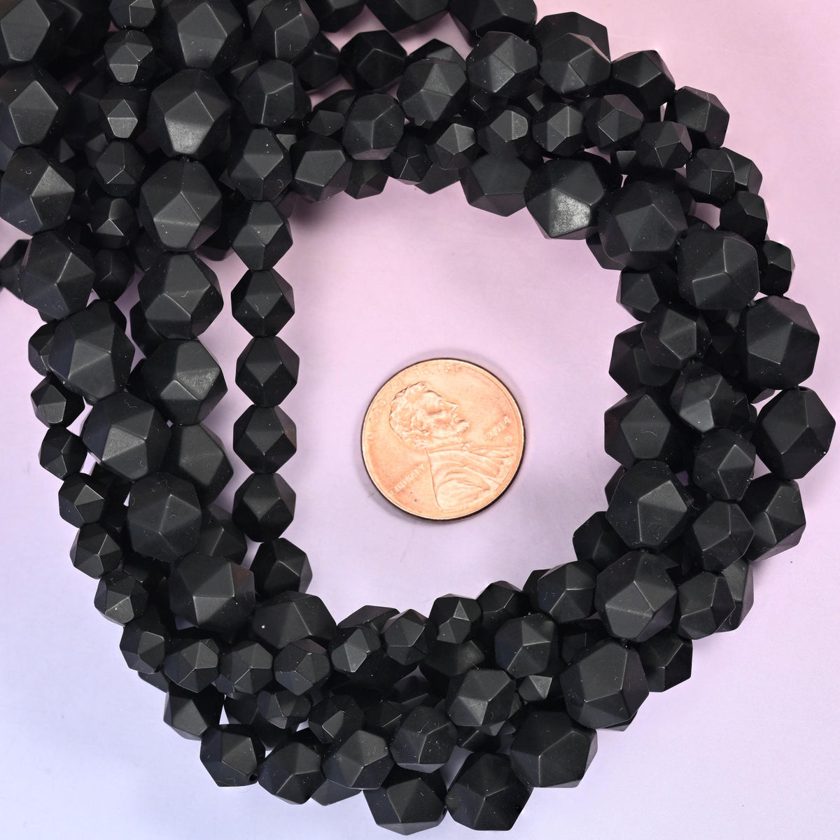 Matte black onyx faceted diamond star cut bead strands coiled around a US penny for size reference