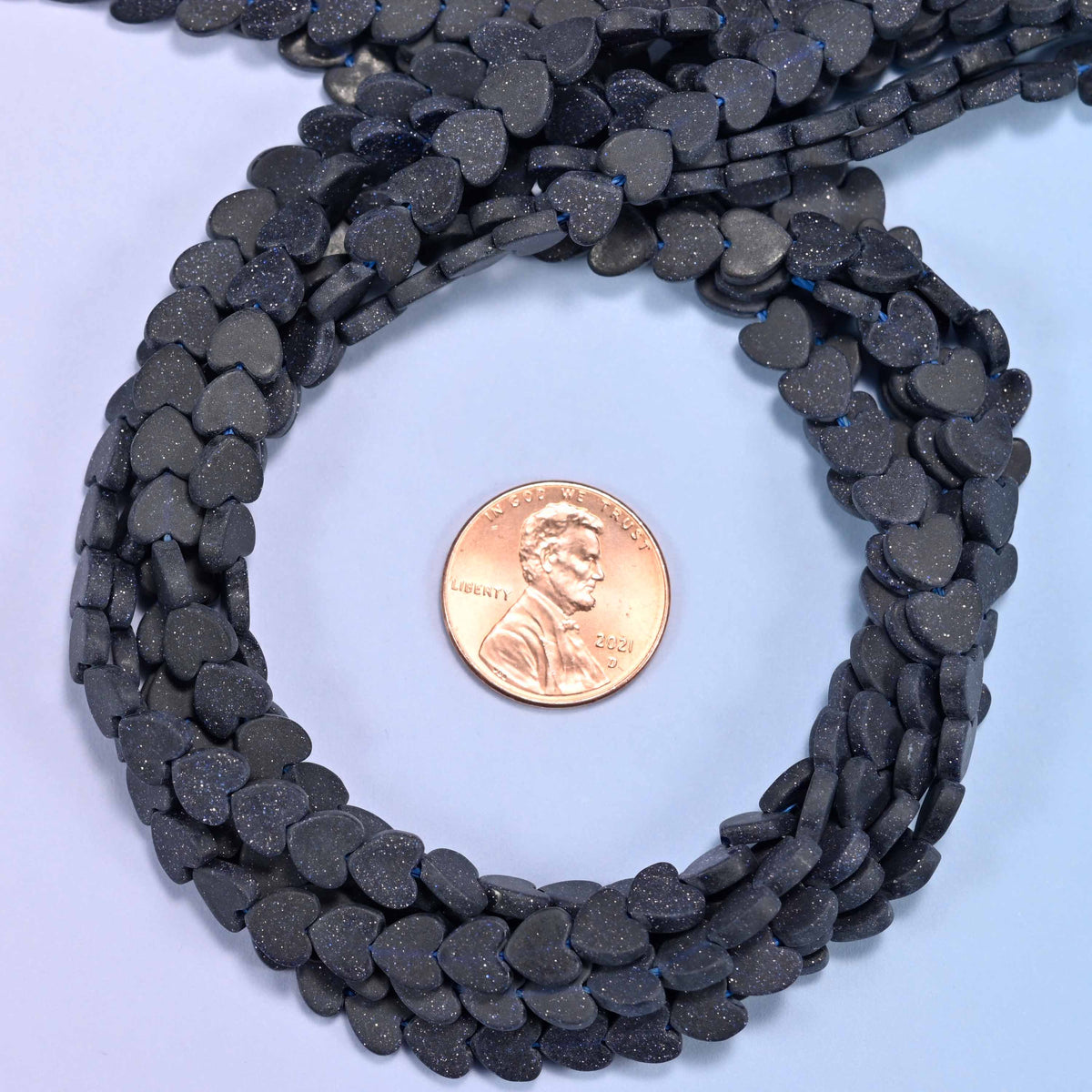 Matte Blue Sandstone flat heart bead strands coiled around a US penny for size reference
