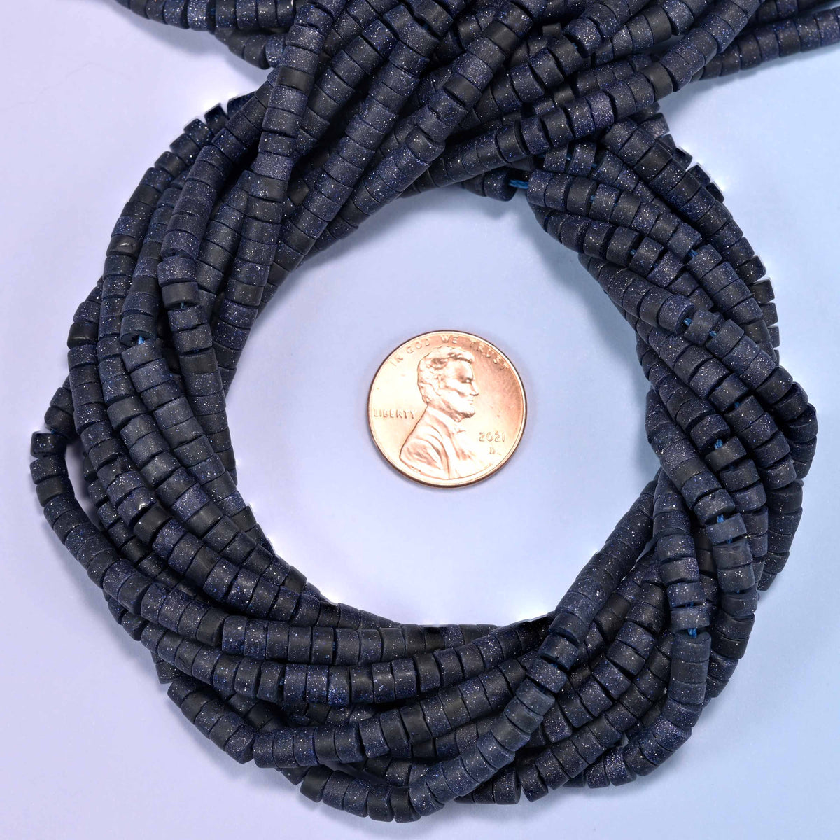 Matte Blue Sandstone heishi disc bead strands coiled around a US penny for size reference